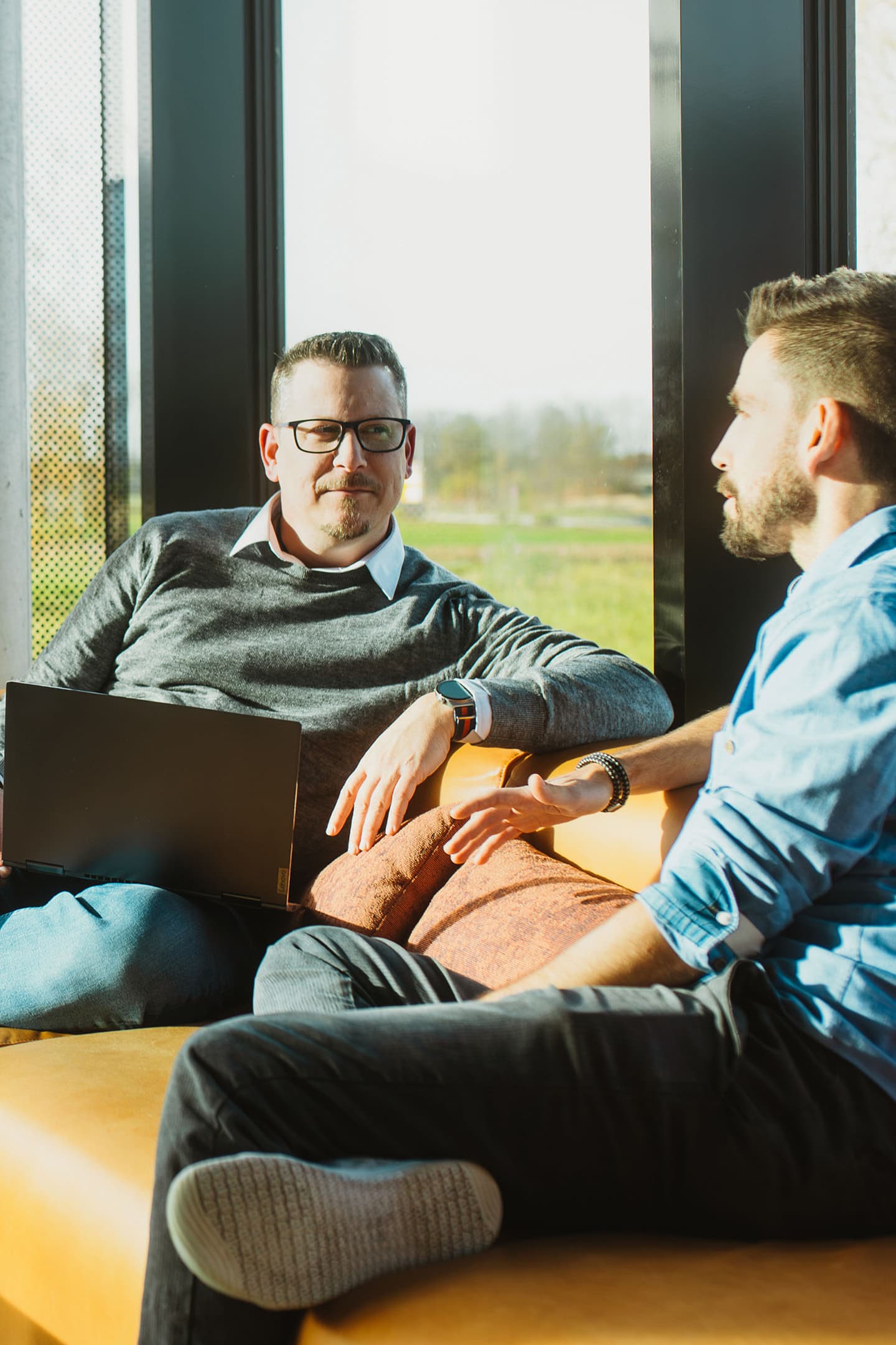 Zwei Kollegen besprechen IT-Management mit einem Laptop in einer hellen Lounge.