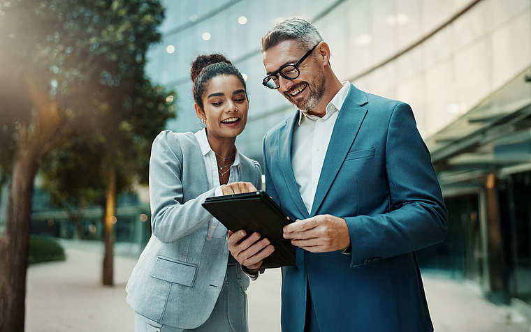 Managerin und Manager analysieren gemeinsam Daten auf einem Tablet – DEX ermöglicht fundierte strategische Entscheidungen
