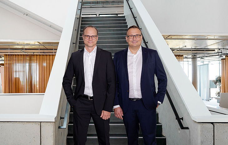 Die Geschäftsführer Michael Huber und Lars Rippert von baramundi stehen vor einer Treppe in einem modernen Bürogebäude